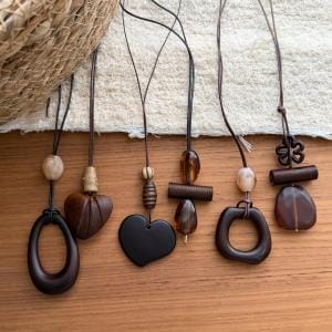 Handgefertigte Halsketten aus Olivenholz mit verschiedenen Anhängern auf einem Holztisch.