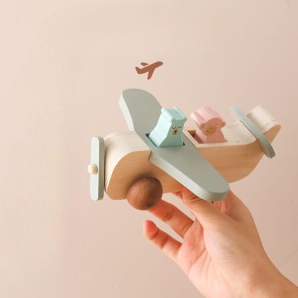 Holzspielzeugflugzeug mit niedlichen Tierpassagieren. Eine Kinderhand hält das pastellfarbene Schiebe- und Flugflugzeug.