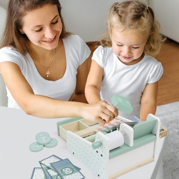 Mutter und Tochter spielen mit einer hölzernen Spielzeugkasse, komplett mit Scanner und Zubehör.