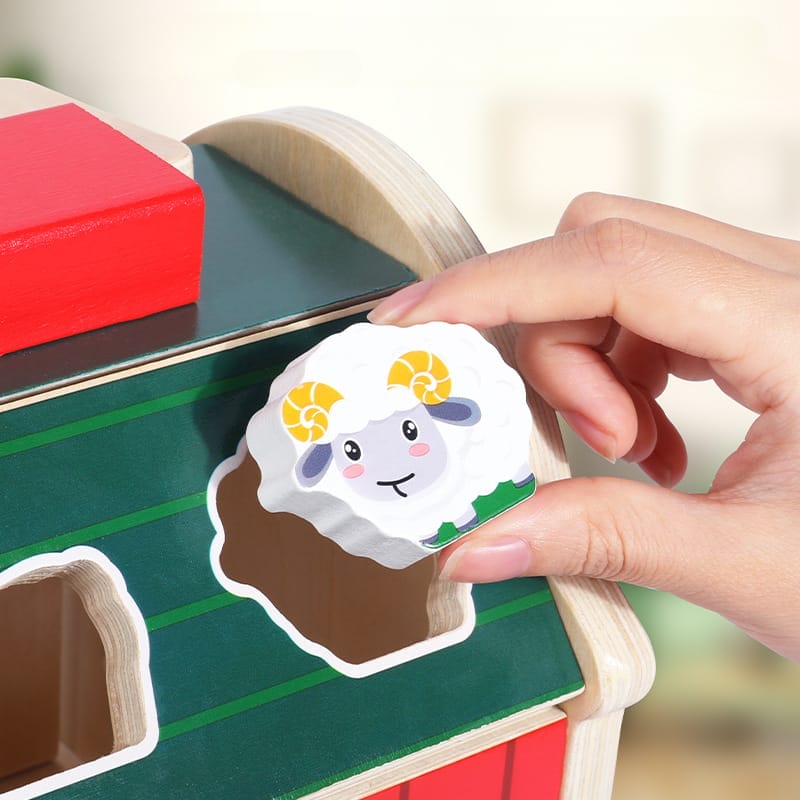 Eine Kinderhand legt ein Holzschaf in einen Formsortierer, Teil eines hölzernen Bauernhofspielzeugs.