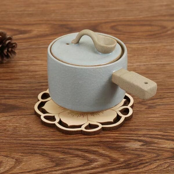 Hellblaue Teetasse aus Keramik mit Deckel und Henkel auf einem lotusförmigen Untersetzer aus Holz.