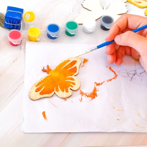 Handbemalter orangefarbener Schmetterling auf unfertigem Holzausschnitt. DIY-Bastelprojekt.