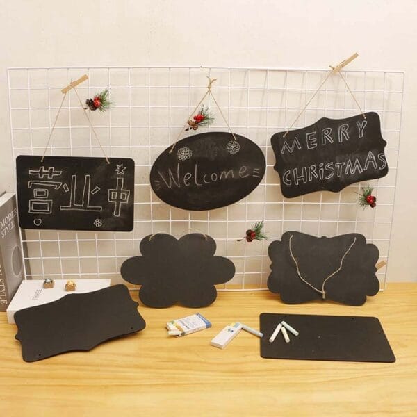 Verschiedene Kreidetafeln hängen an einer Gitterwand. „Willkommen“, „Frohe Weihnachten“ und andere Botschaften stehen darauf. Perfekt für selbstgemachte Deko.