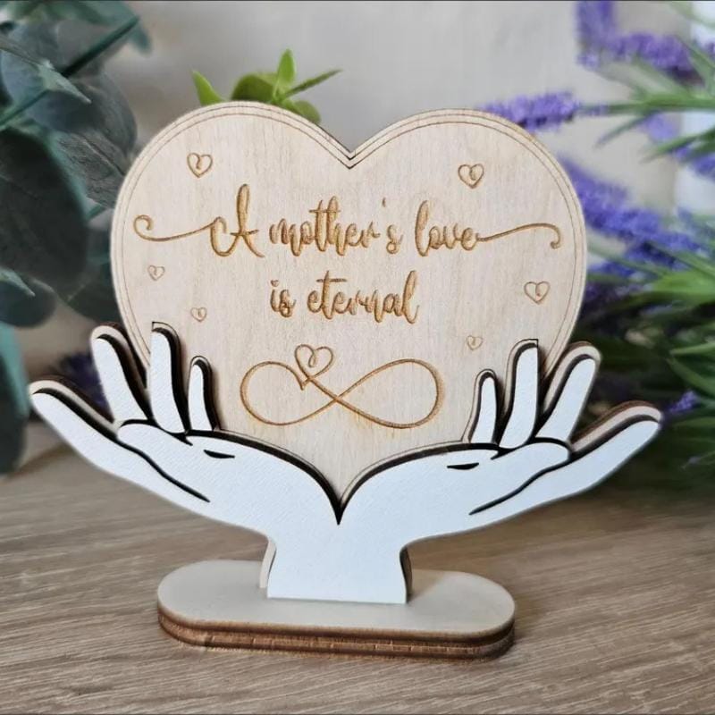 Holzherz mit der Gravur „Die Liebe einer Mutter ist ewig“, von Händen gehalten; Unendlichkeitssymbol.