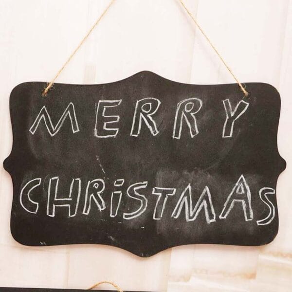 Schwarzes Tafelschild mit der Kreideschrift „Frohe Weihnachten“. An einer Schnur hängend.