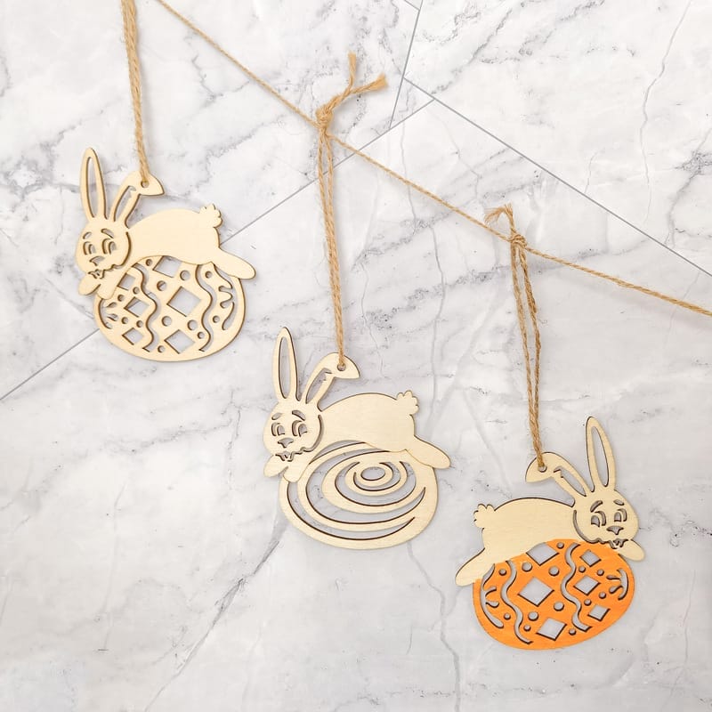 Drei hölzerne Osterhasen-Ornamente mit Juteschnur, perfekt für festliche Dekorationen. Osterhasen im Großhandel erhältlich.