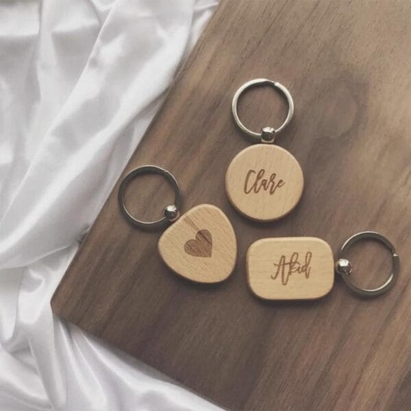 Drei personalisierte Schlüsselanhänger aus Holz: „Clare“, ein Herz und „Abid“. Schlüsselanhänger aus Buchenholz mit Lasergravur.