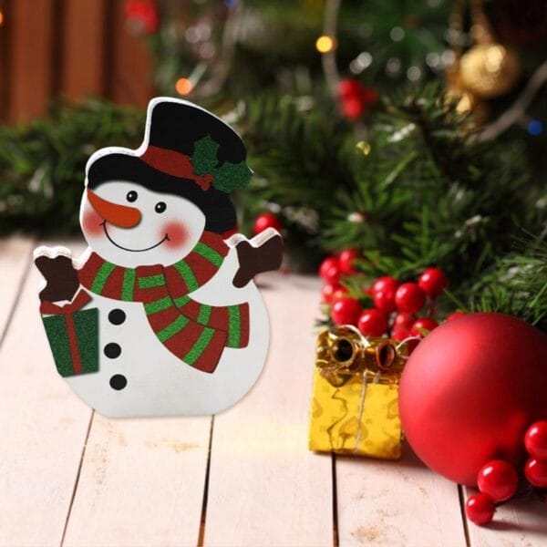 Bezaubernde Weihnachtsdekoration aus Holz in Form eines Schneemanns mit grünem Schal und Geschenk, perfekt für die festliche Tischdekoration.