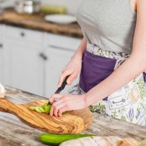 Frau schneidet Gurke auf einem rustikalen Brotzeitbrett aus Holz.