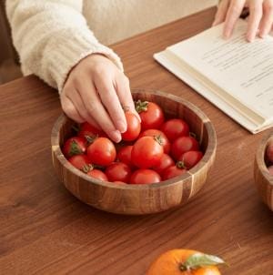 Holzschüssel mit Tomaten, Hand greift nach Tomate. Salatschüssel Holz.