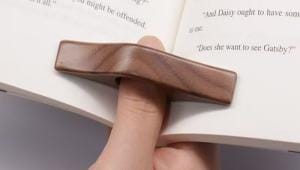 Hand hält einen Daumenseitenhalter aus Walnussholz und hält ein Buch offen. Holz-Lesezeichen.