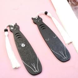 Zwei schwarze Katzenlesezeichen aus Holz mit weißen Quasten.