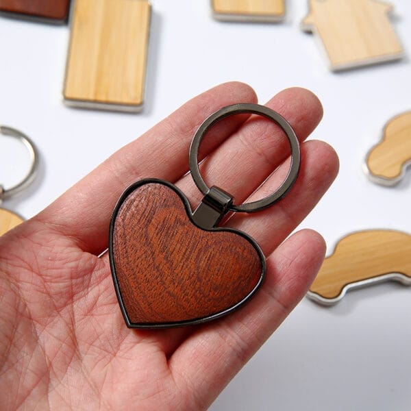Hand hält einen hölzernen Herz-Schlüsselanhänger mit Metallrand. Großhandel mit hölzernen Herz-Schlüsselanhängern.