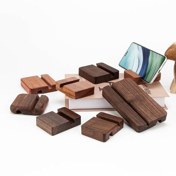 Verschiedene Smartphone-Ständer aus Holz, unter anderem aus Walnuss und Mahagoni, auf einem Buch präsentiert. Stilvolle Handyhalter im Großhandel.