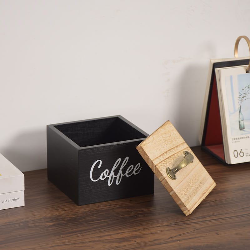Schwarze Kaffee-Aufbewahrungsbox aus Holz mit hellem Holzdeckel und Metallgriff. Auf der Box steht „Coffee“.