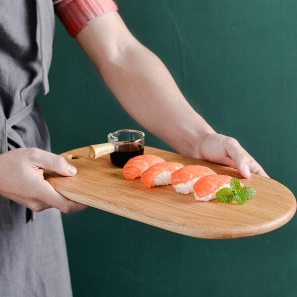 Person präsentiert elegantes Sushi-Brett aus Eiche mit Lachs-Nigiri und Sojasauce.