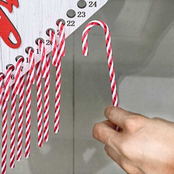 Handauswahl eines Zuckerstangens aus einem hölzernen Weihnachts-Countdown-Kalender mit nummerierten Fächern. Weihnachtsdekoration im Großhandel.