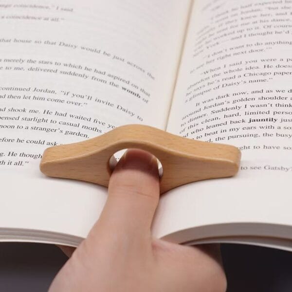 Hand, die einen hölzernen Daumenseitenhalter zum Lesen eines Buches verwendet. Großhandelslesezeichen aus Holz.