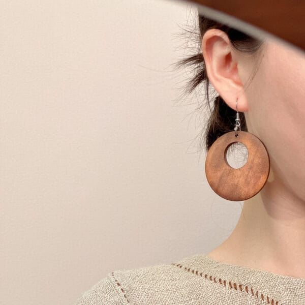 Frau trägt große, braune runde Ohrringe aus Holz. Schmuck im Ethno-Stil.