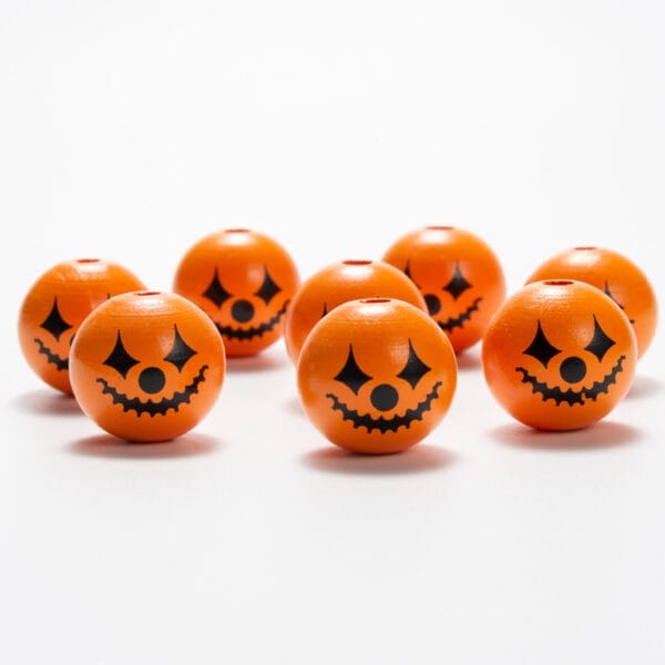 Sieben orangefarbene Halloween-Holzperlen mit Kürbisgesichtern. DIY-Bastelperlen.