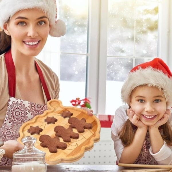 Lächelnde Mutter und Tochter mit Weihnachtslebkuchenmännern auf einem Bambustablett mit Weihnachtsmann-Snacks. Weihnachts-Serviertablett im Großhandel.