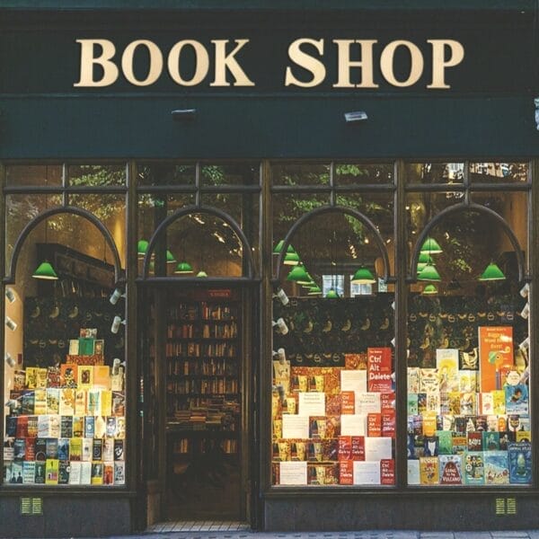 Buchladenfassade mit großem „BOOK SHOP“-Schild. In den Fenstern sind viele Bücher zu sehen.