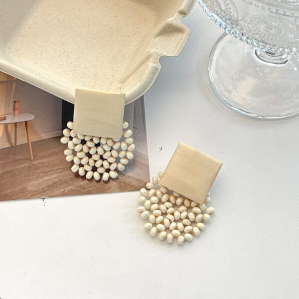 Cremefarbene Perlenohrringe mit geometrischen Holzakzenten. Großhandelsohrringe aus Holz.
