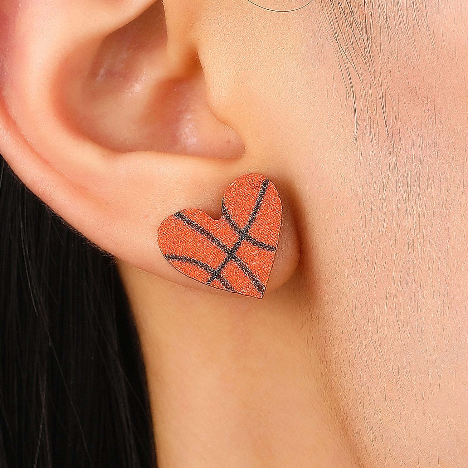 Frau trägt orangefarbene herzförmige Holzohrringe in Basketballform.