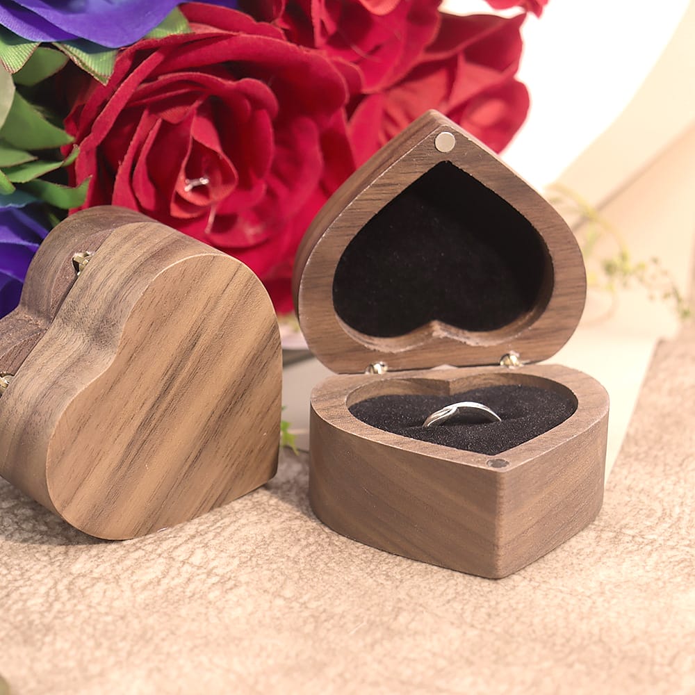 Herzförmige Ringschatulle aus Walnussholz mit einem Silberring, eingebettet zwischen roten Rosen. Perfekt für Verlobungen.