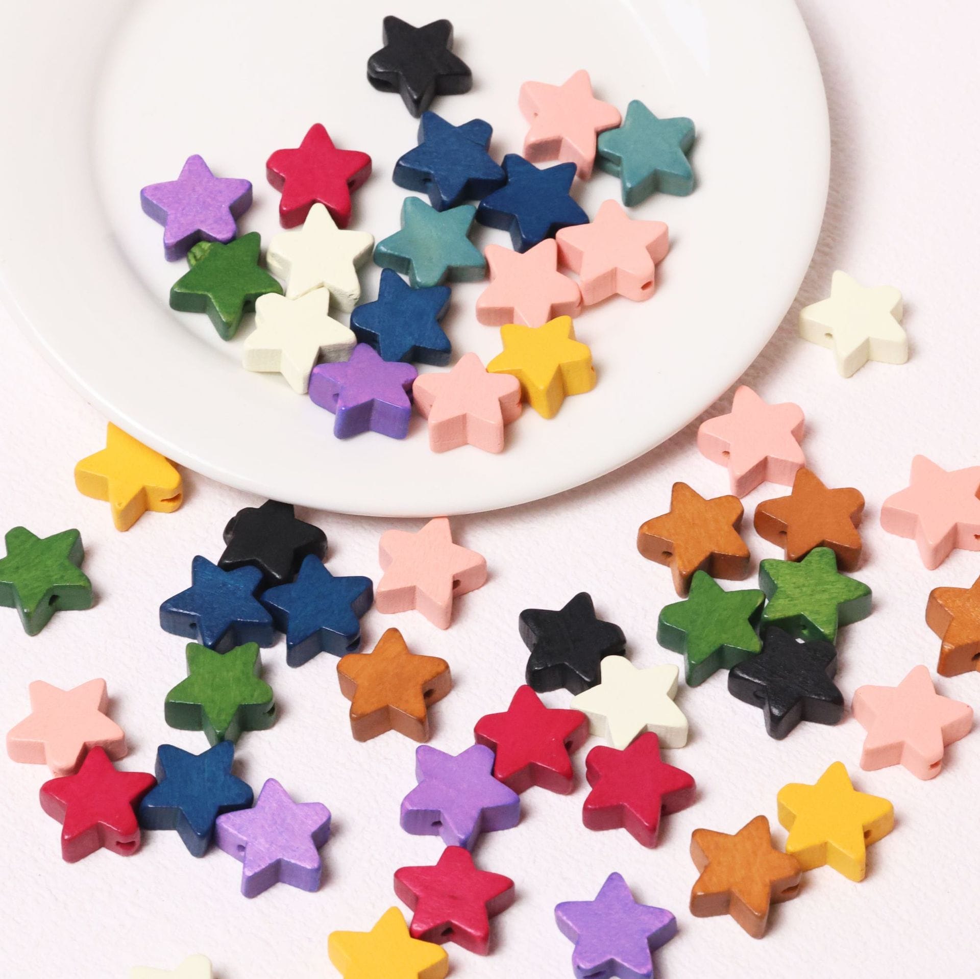 Bunte Stern Holzperlen auf einem weißen Teller verstreut. Großhandelsperlen mit fünfzackigen Sternen zum Basteln.