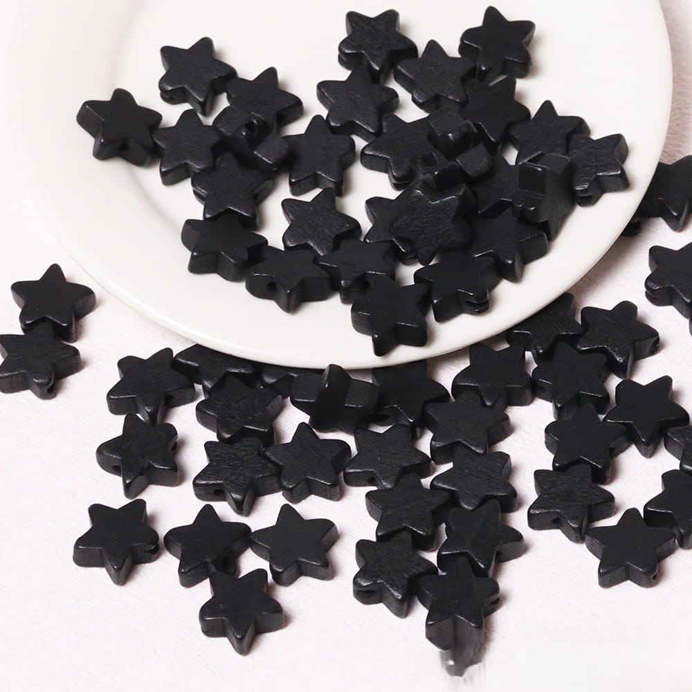 Schwarze Holzsternperlen auf einem weißen Teller und einer weißen Oberfläche verstreut. Großhandels-Holzsternperlen für DIY-Projekte.