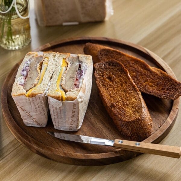 Rundes Serviertablett aus Akazienholz mit Sandwiches und Brot. Stilvolle Holzplatte, perfekt für Snacks und Getränke.