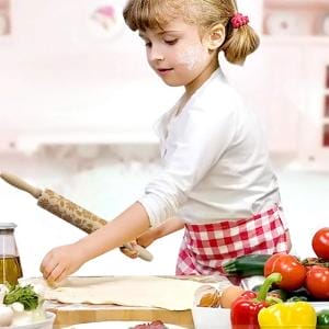 Mädchen rollt Teig aus, Teigrolle mit Muster im Hintergrund.