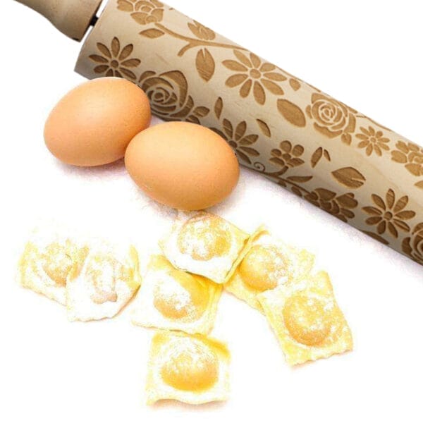 Geprägtes Nudelholz aus Holz mit Blumenmuster, neben Eiern und Ravioli.