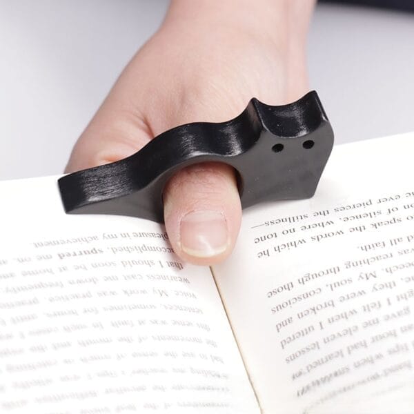 Schwarzer, katzenförmiger Daumenseitenhalter auf einem Buch. Holz-Lesezeichen.