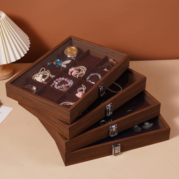 Gestapelte Schmuckkästchen aus Holz mit Glasdeckeln, in denen verschiedene Accessoires präsentiert werden. Walnuss-Finish.