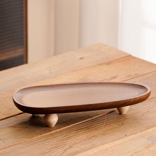 Langes, ovales Serviertablett aus Akazienholz mit kurzen, hellen Holzfüßen. Perfekt für Snacks.