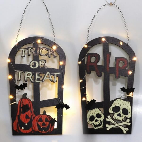 Zwei beleuchtete Halloween-Fensterdekorationen: Eine mit Kürbissen und der Aufschrift „Trick or Treat“, die andere mit Totenköpfen und der Aufschrift „RIP“. Gruselige Friedhofsdekoration.