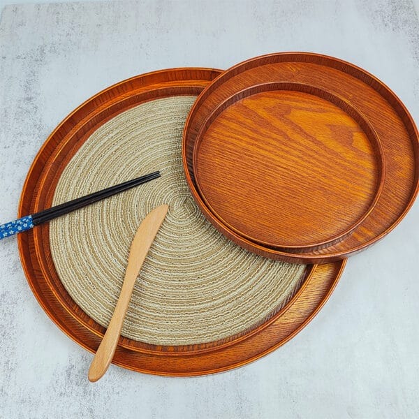 Drei runde Holztabletts, ineinander geschachtelt, mit Essstäbchen und Buttermesser. Japanische Servierplatten, Erlenholz.
