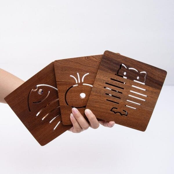 Hand hält drei dunkelbraune, quadratische Untersetzer aus Holz mit ausgeschnittenen Tiermotiven. Untersetzer aus Ebenholz.