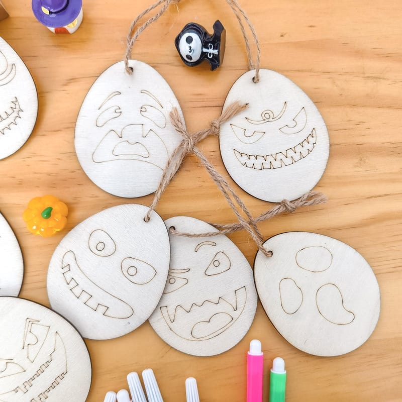 Hölzerne Halloween-Eier-Ornamente mit gruseligen Gesichtern, bereit für die selbstgemachte Dekoration durch Kinder.