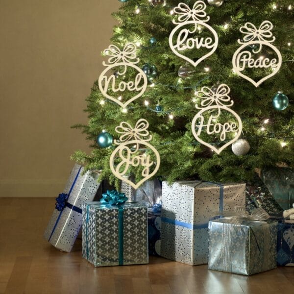 Hölzerner Weihnachtsschmuck mit den Worten „Liebe“, „Frieden“, „Hoffnung“, „Freude“ und „Weihnachten“ hängt an einem geschmückten Baum.