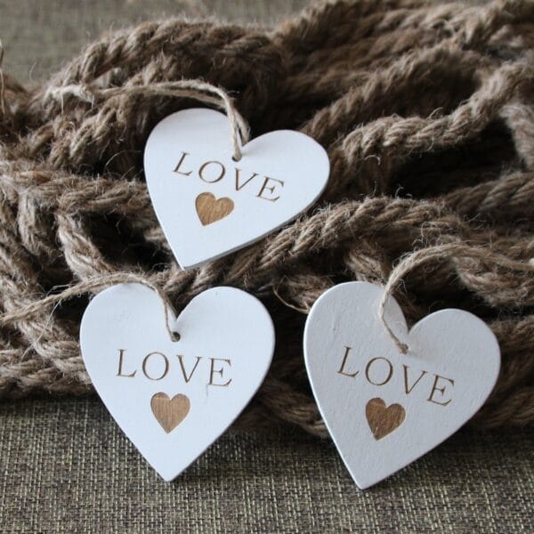 Drei weiße Holzherzen mit der Gravur „LOVE“, perfekte Hochzeits- oder Partydekoration.