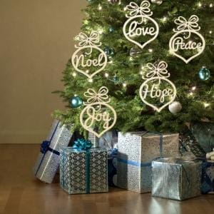 Hölzerner Weihnachtsschmuck mit den Worten „Liebe“, „Frieden“, „Weihnachten“, „Hoffnung“ und „Freude“ an einem geschmückten Baum.