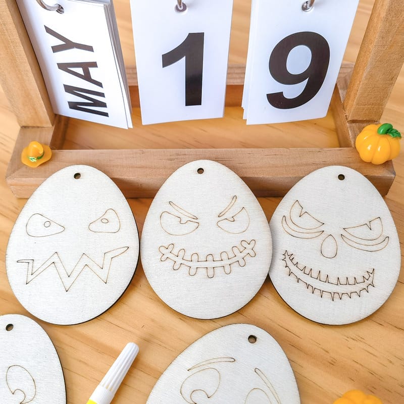 Hölzerne Halloween-Geisterornamente mit dem Kalender vom 19. Mai im Hintergrund. DIY-Bastelarbeit für Kinder.
