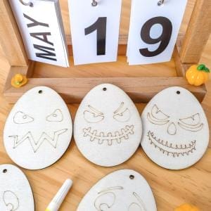 Hölzerne Halloween-Geisterornamente zum Selberbasteln für Kinder. Niedliche, gruselige Gesichter, die in eiförmige Holzscheiben eingraviert sind.