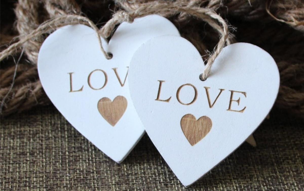 Zwei weiße Holzherzen mit der Gravur „LOVE“, perfekte Hochzeits- oder Partydekoration.