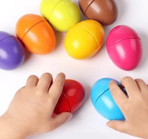 Kinderhände spielen mit bunten Montessori-Holzeiern. Ideal zur Farb- und Formerkennung.