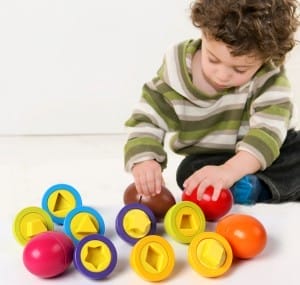 Kleinkind spielt mit bunten Eiern zum Formensortieren. Montessori-Holzspielzeug zum Erkennen von Farben und Formen.