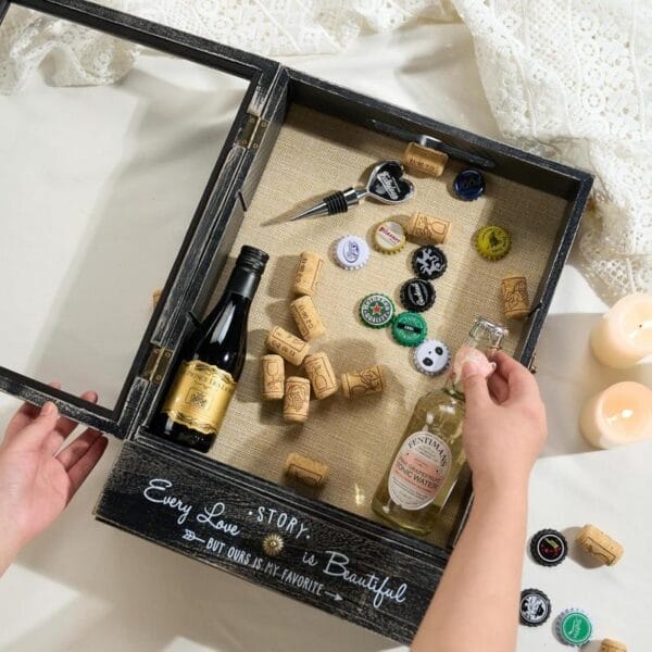 Dekorative Holzbox mit Glasdeckel, gefüllt mit Weinkorken, Kronkorken und Mini-Weinflaschen. Der Text lautet: „Jede Liebesgeschichte ist schön“.